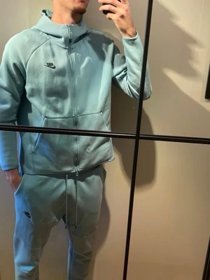 Ljusblå mjukisbyxor från Nike - Snygga ljusblå mjukisbyxor från Nike med dragsko i midjan och diskret logga på benet. Byxorna har en avslappnad passform och är tillverkade i mjukt material som känns skönt mot huden. Perfekta för en chill och sportig stil.