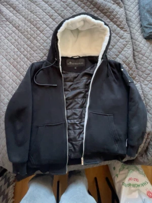Svart pufferjacka Moose Knuckles - Säljer en svart pufferjacka från Moose Knuckles med vit, fluffig foder i huvan och quiltad insida. Jackan har dragkedja, två fickor framtill och ribbade muddar. Perfekt för kalla vinterdagar och riktigt snygg streetstil. Fraktar alltid samma dag eller dagen efter