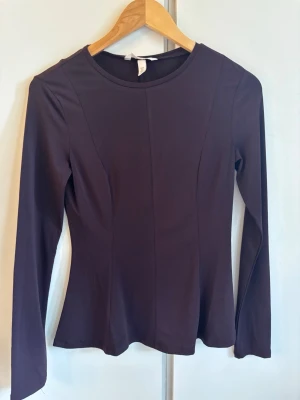 Mörklila långärmad topp från H&M - Säljer en stilren mörklila långärmad topp från H&M. Toppen har en figurnära passform och rund halsringning. Perfekt att matcha med jeans eller kjol för en snygg look.