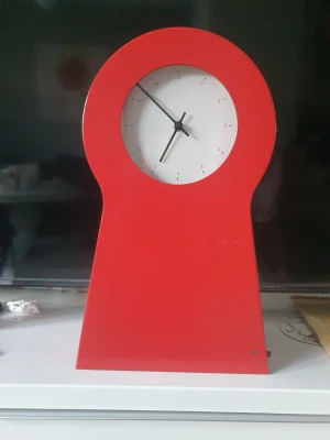 Röd modern bordsklocka/ eller vägg - Säljer en stilren bordsklocka i röd plast med unik, modern form. Klockan har en vit urtavla med svarta visare och minimalistiska siffror. Perfekt som inredningsdetalj för dig som gillar färg och design.
