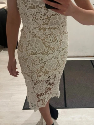 Vit spetsklänning med blommönster - Supersnygg vit spetsklänning med blommigt mönster och figurnära passform. Klänningen har en kort längd och är perfekt för sommarens alla tillfällen. Detaljerad spets ger en romantisk och trendig look.