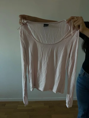 Ljusrosa långärmad topp Gina Tricot - Säljer en ljusrosa långärmad topp från Gina Tricot. Toppen har en rund, djup urringning och tunna axelband som detalj. Tillverkad i mjuk bomull, perfekt för en enkel och stilren look.