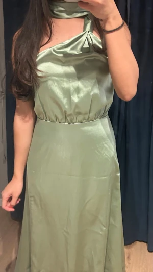 Ljusgrön långklänning i satin - Snygg ljusgrön långklänning i glansigt satinmaterial från Cider i stl XS. Klänningen har markerad midja och ett elegant, flytande fall. Perfekt för dig som vill sticka ut med en modern och chic look. ALDRIG ANVÄND