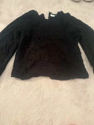 Svart blus med 3D-blommor från Vila - Snygg svart blus från Vila med långärmad design och coola 3D-blommor över hela tyget. Blusen har en rak passform och hög hals, endast använd 1 gång så i mycket bra skick!
