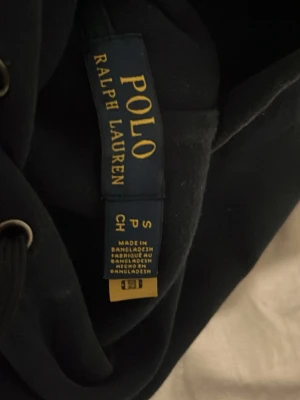 Svart hoodie från Polo Ralph Lauren - Klassisk navy hoodie från Polo Ralph Lauren med den ikoniska vita broderade loggan på ärmen. Hoodien är tillverkad i mjukt material som känns skönt mot huden. Perfekt för en avslappnad och stilren look.