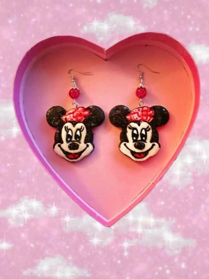 Mimmi Pigg örhängen med pärldetalj - oanvända  - Unika örhängen med Mimmi Pigg-motiv i svart, vitt och rött. Örhängena har en röd pärla ovanför motivet och krokar i silverfärg. Perfekta för dig som älskar Disney och vill sticka ut med färgglada accessoarer. då jag själv gör dom får man nya och oanvända 