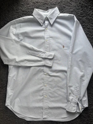 Oanvänd Ralph Lauren Skjorta LT Tall Randig Blå/Vit - Lyxig Ralph Lauren skjorta! Tidlös look med oslagbar premiumkvalitet. Kvitto finns ej, men den är helt oanvänd, endast testad. 👕 Ralph Lauren - Button-Down 🪡 LT Tall – Regular Tall Fit 🧵 100% Bomull – Kvalité, oxford-tyg 📐 Mått: Bröst: 64 cm Längd: 83 cm Ärm: 57 cm (från armhåla) ✅ 10/10 – Nyskick, oanvänd. Tags saknas. ✨ Knappkrage, Bröstficka, Manschettknappar 💰 Ca 1400 kr ‼️ Skickas inom 24h ‼️