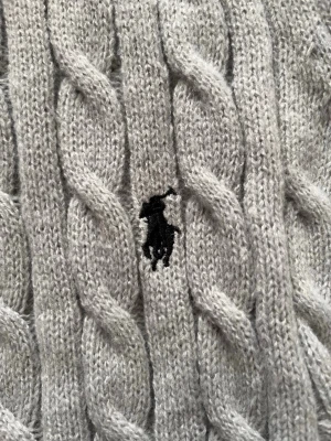 Polo Ralph Lauren  Quaterzip  - Snygg ljusgrå quaterzip  från Polo Ralph Lauren med halv dragkedja och ribbade muddar. Tröjan har det klassiska broderade logotypen på bröstet och är tillverkad i mjukt material. Perfekt för lager på lager och en clean look.