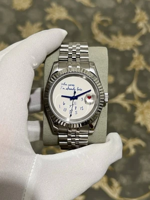 Silverfärgad Seiko datejust mode - Unik Seiko klocka i silver med länkarmband i rostfritt stål. Urtavlan har handskriven text 'Who cares I'm already late' och siffrorna är utspridda, med ett hjärta vid klockan 3. Genomskinlig baksida som visar urverket. Perfekt för dig som gillar personliga detaljer.