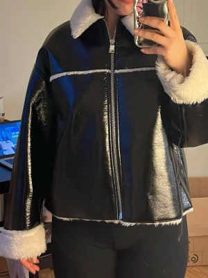 Svart pälsjacka med vita detaljer - Säljer en svart pälsjacka med vita, fluffiga detaljer vid krage, ärmslut och nederkant. Jackan har en rak passform, dragkedja framtill och kontrasterande sömmar. Perfekt för dig som vill ha en trendig och varm vinterjacka.