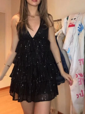 Svart glittrig volangklänning - Supersnygg svart kortklänning med glittriga paljetter och flera lager volanger och öppen rygg. I super bra skick!💕