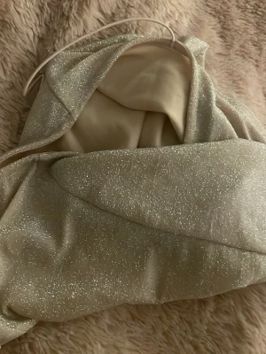 Glittrig guldig festtopp - Säljer en snygg glittrig linnetopp i silver med smala axelband. Toppen har en enkel och stilren form, perfekt för att sticka ut. Materialet är syntet och har en skimrande finish som ger en cool look.