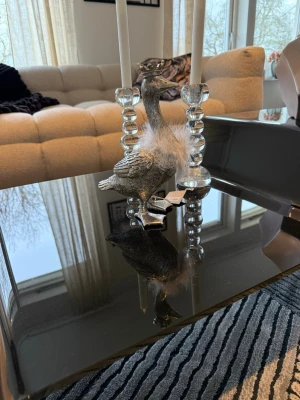 Dekorativ silverfärgad gås med krona - Säljer en dekorativ gås i silverfärgat material med en liten krona på huvudet och fluffiga vita fjädrar runt halsen. Perfekt som inredningsdetalj på soffbordet eller hyllan. Gåsen är gjord av Lene Bjerre  