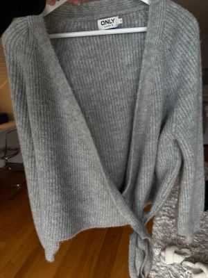 Grå ribbstickad omlottkofta från ONLY - Mjuk och ribbstickad grå omlottkofta från ONLY med knytband i midjan. Super skön och väldigt fin passform 🩷