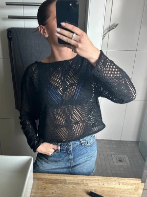 Svart virkad topp tröja  - Säljer en svart  virkad topp med lång ärm och genombrutet mönster. Toppen har en loose passform och är perfekt att styla över ett linne eller bikini. Ger en cool och avslappnad vibe till din outfit.