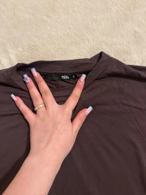 Brun croppad t-shirt från 157 - Säljer en enkel brun croppad t-shirt från 157. T-shirten har korta ärmar, rund halsringning och är gjord i mjuk bomull. Perfekt till jeans eller kjol för en chill look.