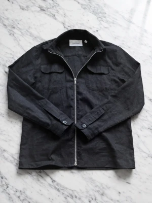 Svart overshirt - Hej! Säljer nu denna svarta overshirt då den inte kommer till andvändning så mycket. Den passar perfekt nu till våren och sena sommarkvällar! Den är i toppen skick inga defekter eller nästan tecken på andvändning kvitto finns även kvar. Om du har några frågar är de bara att ställa, pris kan diskuteras