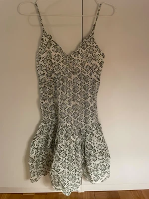 Blommig sommarklänning - Supersöt vit klänning med grönt blommönster.  Smala axelband, Klänningen har v-ringad urringning och volang nedtill. Tillverkad av 100% bomull.på baksidan av klänningen finns det en dragkedja. Denna klänning är perfekt för varma dagar ☀️