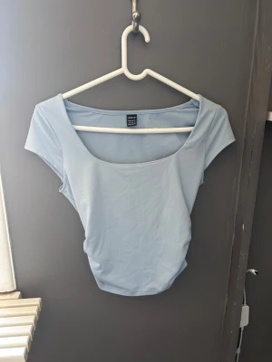 Ljusblå croppad topp - Snygg ljusblå croppad topp med bred, rundad urringning och korta ärmar. Tillverkad i mjuk bomullsmix som sitter tight och framhäver figuren. 