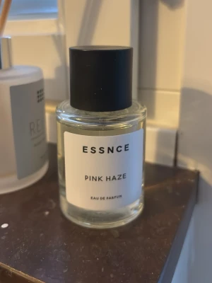ESSNCE Pink Haze Eau de Parfum - Endast sprayad för att känna doften, helt ny. Fräsch parfym från ESSNCE med namnet Pink Haze. Flaskan är cylindrisk i genomskinligt glas med svart rund kork och stilren vit etikett. Doften är en Eau de Parfum och passar dig som gillar moderna, minimalistiska parfymer.