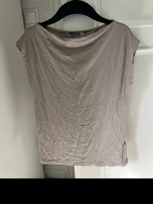 Beige topp - En basic beige topp, lite draperad framtill beroende på kroppsform. Toppen är ärmlös och tillverkad i mjukt material. Färgen liknar mest den på första bilden.