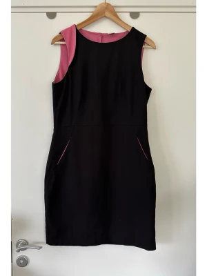 Svart ärmlös klänning med rosa detaljer, VERO MODA, 38 / M - Stilren svart figursydd klänning med rosa detaljer från Vero Moda i storlek M / 38. Klassisk ärmlös modell med en rund halsringning. Den har fickor i sidorna med rosa foder som matchar de rosa detaljerna vid halsen. Klänningen stängs med två knappar i nacken. Fodrad med tunt foder och smickrande diskreta insydda detaljer i midjan för bästa passform. Superfin klänning som tyvärr är för liten för mig nu. Mycket gott skick, som ny!