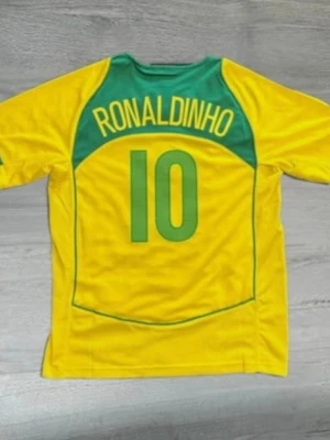 Braziltröja 2004-06  - Säljer en ikonisk gul Brasilien fotbollströja med gröna detaljer och Ronaldinho samt nummer 10 på ryggen. Perfekt för dig som älskar fotboll och vill sticka ut på planen eller läktaren. Tillverkad i lätt och ventilerande material.
