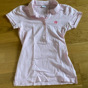 Ljusrosa pikétröja - Söt ljusrosa pikétröja med korta ärmar och klassisk krage. Tröjan har knappar framtill och en broderad mörkrosa krona på vänstra bröstet. Den är från Gina tricot!! Köpt här på plick men har inte kommit till användning🩷