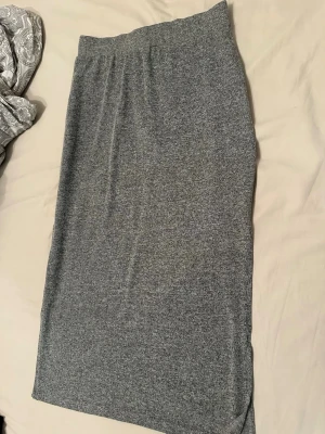 Grå långkjol i mjukt material - En enkel och stilren grå långkjol med rak passform. Kjolen är gjord i ett mjukt och stretchigt material som känns bekvämt mot huden. Perfekt att matcha med en crop top eller hoodie för en avslappnad look.