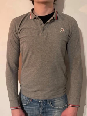 Moncler Långermad Piké  - | Skick: 9/10 | Färg: Grå | Modell: 172cm 62kg | Vad inkluderas: Enbart pinetröjan | Nypris: 3 999kr |