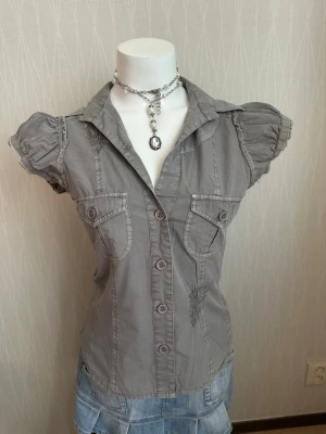  kortärmad blus med puffärm -  blus med puffärmar och knappar framtill. Två bröstfickor med lock och dekorativa sömmar ger en cool look. Skjortkrage och figurnära passform. Perfekt till jeans eller kjol för en trendig stil.