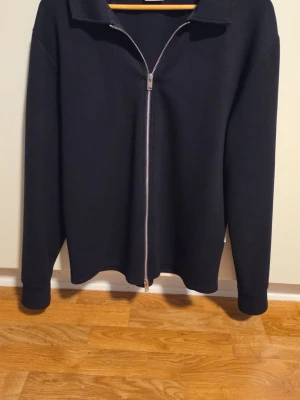 Svart ziptröja från Selected Homme - Snygg svart ziptröja från Selected Homme med hel dragkedja framtill och klassisk krage. Tröjan har långa ärmar och är tillverkad i ett mjukt material som passar perfekt till lager på lager. Enkel och stilren design som funkar till det mesta.