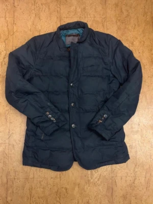 Mörkblå Massimo Dutti jacka - Stilren mörkblå pufferjacka med knäppning framtill och quiltad design. Jackan har ståkrage, knappdetaljer vid ärmsluten och två sidofickor. Perfekt för kalla dagar och ger en clean look. Fodrad insida för extra värme.