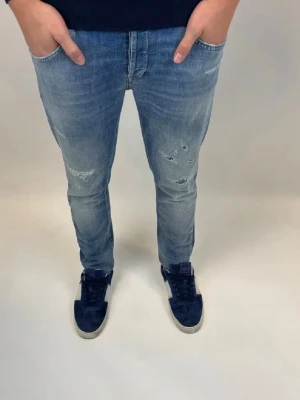 Blå slitna jeans - Snygga blå jeans med slitningar på knäna och lätt tvättad look. Jeansen har klassisk femficksdesign och smal passform som sitter tajt längs benen. Perfekta för en avslappnad och trendig stil.