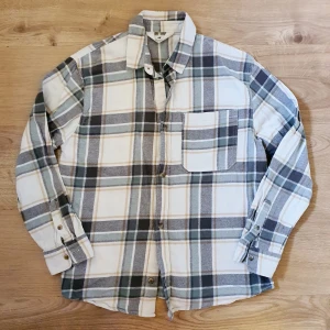  Flanellskjorta stl 152 - Klassisk rutig flanellskjorta från H&M i mjuk bomull. Skjortan har långa ärmar, bröstficka och knappar framtill. Färgkombinationen går i vitt, grått och beige med inslag av grönt. Mycket bra skick! Storlek 152 cm, ca 11-12 år (juniorstl M).