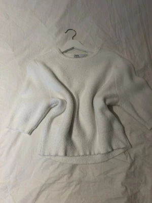 Vit stickad tröja från Zara - Mysig vit stickad tröja från Zara med rund halsringning och halvlånga ärmar. Tröjan har en något boxig passform och ribbstickade muddar vid ärmslut och nederkant. Perfekt för lager på lager och enkel att styla till olika looks.