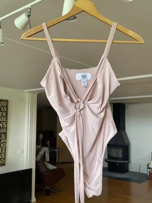 Beige body från Rebecca Stella - Säljer en supersnygg body/baddräkt från Rebecca Stella i ljus rosa/nude färg. Modell med djup urringning och silverfärgad ringdetalj framtill. Väldigt smickrande passform och stretchigt material.  Perfekt till semester, strand, festival eller sommaroutfit ☀️  ✨ Storlek: S ✨ Skick: Fint skick ✨ Märke: Rebecca Stella  Perfekt till stranden, semester eller stylad som body till jeans/kjol. Har tvättats!   Ge bud! Pris kan diskuteras såklart.   #RebeccaStella #Baddräkt #Body #Sommar #Bikini #Trendigt 