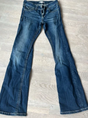 Blå bootcut jeans med kontrastsömmar - Snygga blå bootcut jeans och markerade kontrastsömmar. Jeansen har klassisk femficksdesign, låg midja och utsvängda ben. Perfekta för en avslappnad och trendig look.