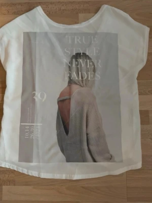 Vit t-shirt med tryck och text - Vit t-shirt med ett stort tryck framtill som föreställer en person bakifrån och texten 'TRUE STYLE NEVER FADES'. T-shirten har rund hals och korta ärmar, perfekt för en avslappnad look. Använd en gång.