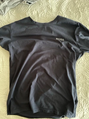Mörkblå BOSS t-shirt i bomull - Snygg mörkblå t-shirt från BOSS i mjuk bomull. Klassisk passform med rund halsringning och diskret BOSS-logga broderad på bröstet. Perfekt för en stilren och enkel look.