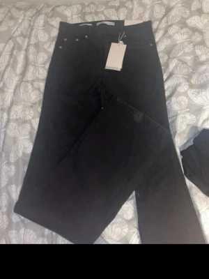 Svarta raka jeans från Bershka - Säljer ett par svarta jeans från Bershka med raka ben och hög midja. Jeansen har klassisk femficksdesign och metallknappar. Perfekta för en clean och stilren look. Materialet är bomull med lite stretch för extra komfort.