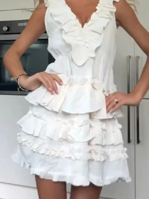 SLUTSÅLD Vit H&M volangklänning  - Supersöt vit klänning med flera volanglager och djup v-ringning. Klänningen är ärmlös och har en romantisk känsla med sina mjuka volanger och omlottliknande detaljer framtill. Perfekt för sommarens alla tillfällen.