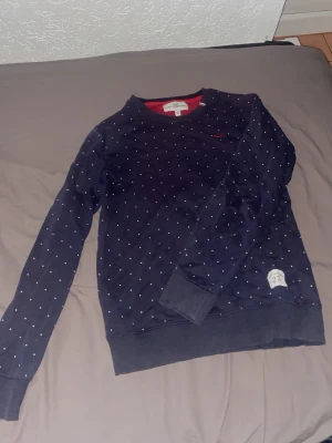 Mörkblå prickig tröja Hampton Republic - Snygg mörkblå sweatshirt från Hampton Republic med små vita prickar och röd broderad logga på bröstet. Tröjan har rund halsringning, ribbade muddar och röd insida vid halsen. Perfekt för en avslappnad och stilren look.