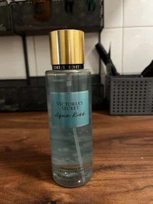Victoria's Secret Aqua Kiss mist - Fräsch body mist från Victoria's Secret i doften Aqua Kiss. Flaskan är genomskinlig med blå etikett och har ett lyxigt guldigt lock. Rymmer 250 ml och har en lätt, vatteninspirerad doft med inslag av fräsch blomma. Perfekt för dig som gillar lätta och fräscha parfymer.