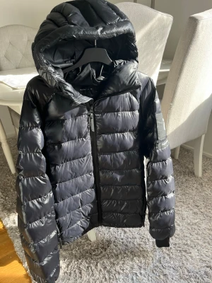 Peak Performance herr dunjacka, svart - Peak Performance herr dunjacka, svart. Glansig modell. Kan se lite mörkblå ut i solen. Storlek M. Fint skick, en defekt i innertyget. Påverkar inte funktionen och syns inte vid användning, se bild. 1000kr