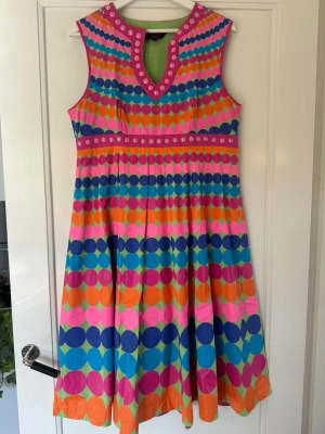 Klänning från Indiska (Manish Arora) - Klänning från Indiskas samarbete med Manish Arora. Sparsamt använd. Superhärlig ärmlös klänning med färgglatt cirkelmönster i rosa, blått, orange och turkos. Klänningen har v-ringning med dekorativa detaljer och en utställd form som ger en lekfull look. Perfekt för dig som vill sticka ut i sommar! Ett litet stygn har gått upp i ena armhålan. Se bild. Lättfixat av den händige. 