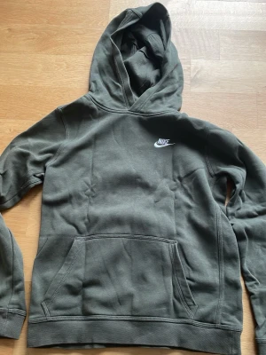 Olivgrön Nike hoodie med huva - Snygg olivgrön hoodie från Nike med klassisk logga på bröstet. Hoodien har en stor känguruficka framtill och en skön huva. 