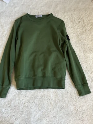 Grön sweatshirt från Stone Island - Snygg grön sweatshirt från Stone Island med klassisk patch på ärmen. Tröjan har rund halsringning och långa ärmar. Perfekt för en avslappnad och trendig stil. Är 10-12