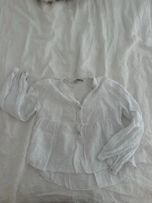 Vit linneskjorta från Zara - Luftig vit blus från Zara i 100% linne med knappar framtill och rundad halsringning. Blusen har lång ärm med knapp vid ärmslut och en avslappnad, något vid passform. Perfekt för en stilren och enkel look.