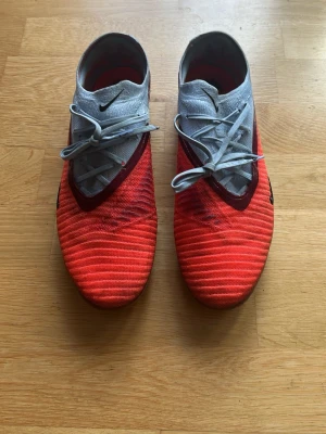 Nike Phantom Elite fotbollsskor storlek 43 - Säljer ett par Nike Phantom Vision fotbollsskor i en snygg kombination av ljusblått och neonorange med svarta detaljer. Skorna har snörning och är designade för bra bollkontroll och grepp på planen. Perfekta för dig som vill sticka ut på matchen. Använda väldigt få gånger, pris kan diskuteras vid snabb affär.